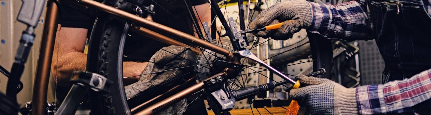 Red head bearded mechanic fixing rear derailleur from a bicycle in a workshop.